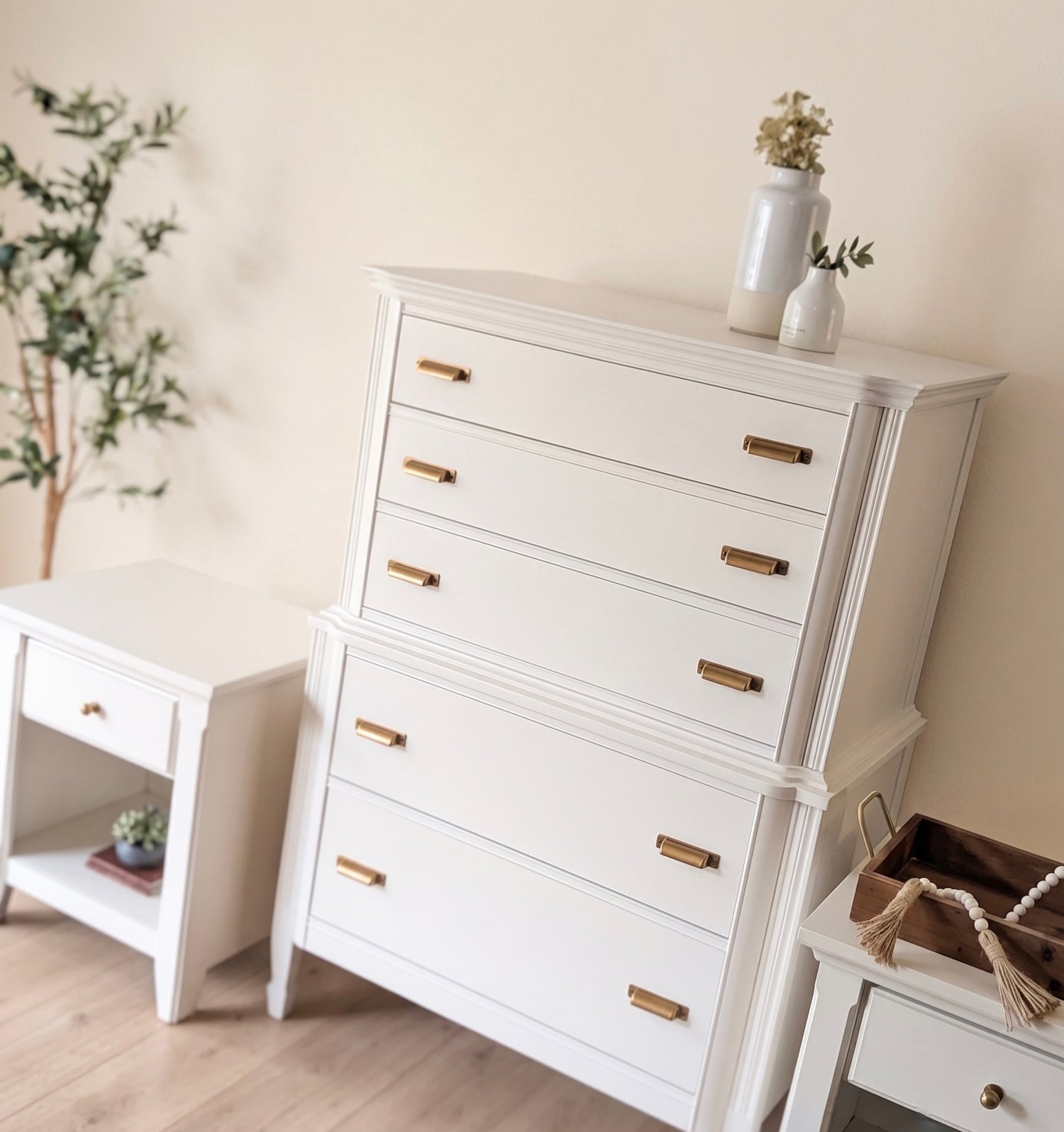 White dresser with gold handles in a room with a plant and small table.